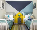 Habitaciones juveniles con camas blancas y pared geométrica en azul, gris y amarillo. Alfombra de rayas y decoración náutica.