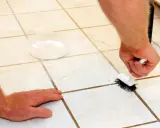 Persona limpiando las juntas del suelo con un cepillo y un recipiente con producto.