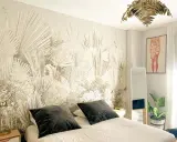Habitación con papel tapiz de palmeras, ideal para aprender cómo empapelar una pared. Cama con almohadas oscuras, espejo y planta.