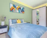 Dormitorio con paredes verde menta y detalles amarillos en el techo. Cama azul, mesita de noche y armario blanco. Inspiración de colores para pintar un dormitorio pequeño.