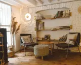 Acogedor rincón de lectura con sillas cómodas, mesa auxiliar, estanterías llenas de libros y plantas secas.
