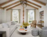Salón luminoso con vigas de madera en el techo, creando la sensación de casas con techos bajos. Sofá blanco, mesa ovalada y butaca a rayas.