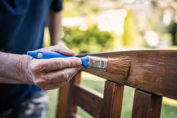Mano aplicando barniz a un banco de jardín, creando un hermoso efecto madera.