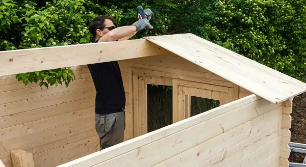 Hombre ensamblando una caseta de jardín con maderas para exterior.