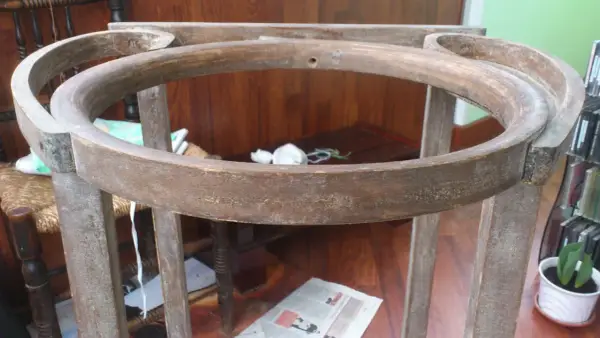 Estructura de madera de un palanganero antiguo, lista para restaurar. Se aprecian sus patas y el aro superior curvo.